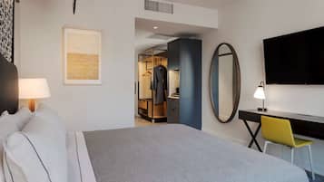A hotel room with a bed, a desk, a chair, a TV, a mirror, and a wardrobe.