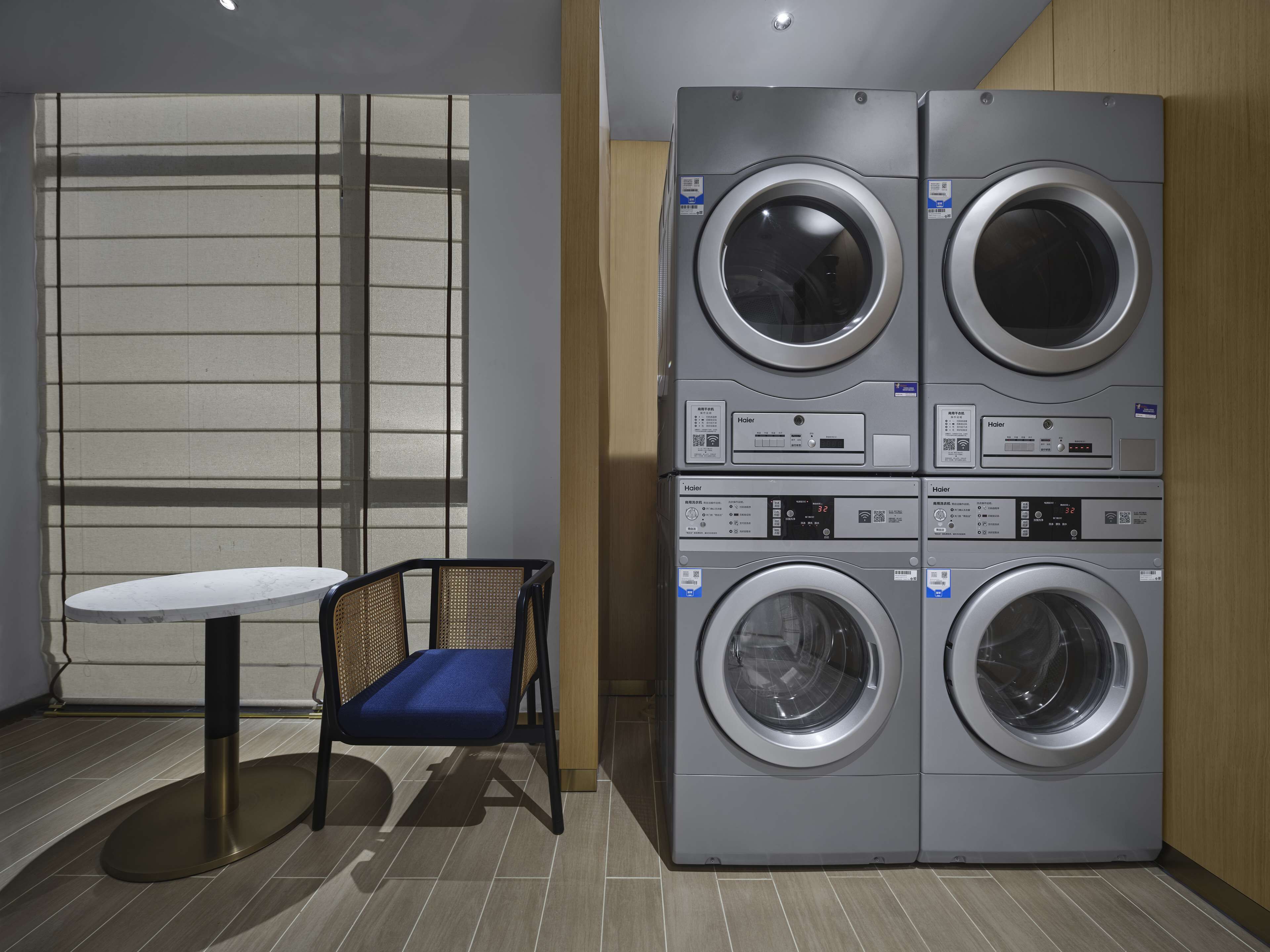 A laundry room with four stacked front-loading washing machines, a small table, and a chair.