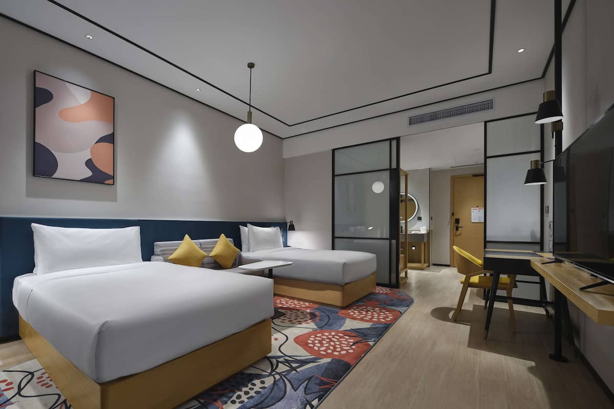 A modern hotel room with two beds, a desk, and a television.