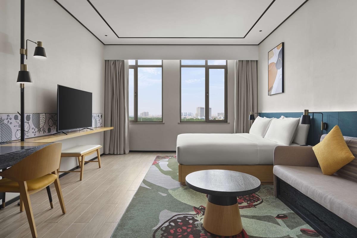 A modern hotel room with a bed, sofa, desk, and TV.