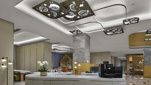 Un hall d’hôtel moderne avec un comptoir d’accueil central, des luminaires contemporains et un sol en marbre.