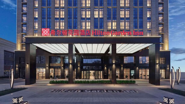 Une entrée d’hôtel moderne, dotée d’un auvent en verre et d’une enseigne lumineuse.