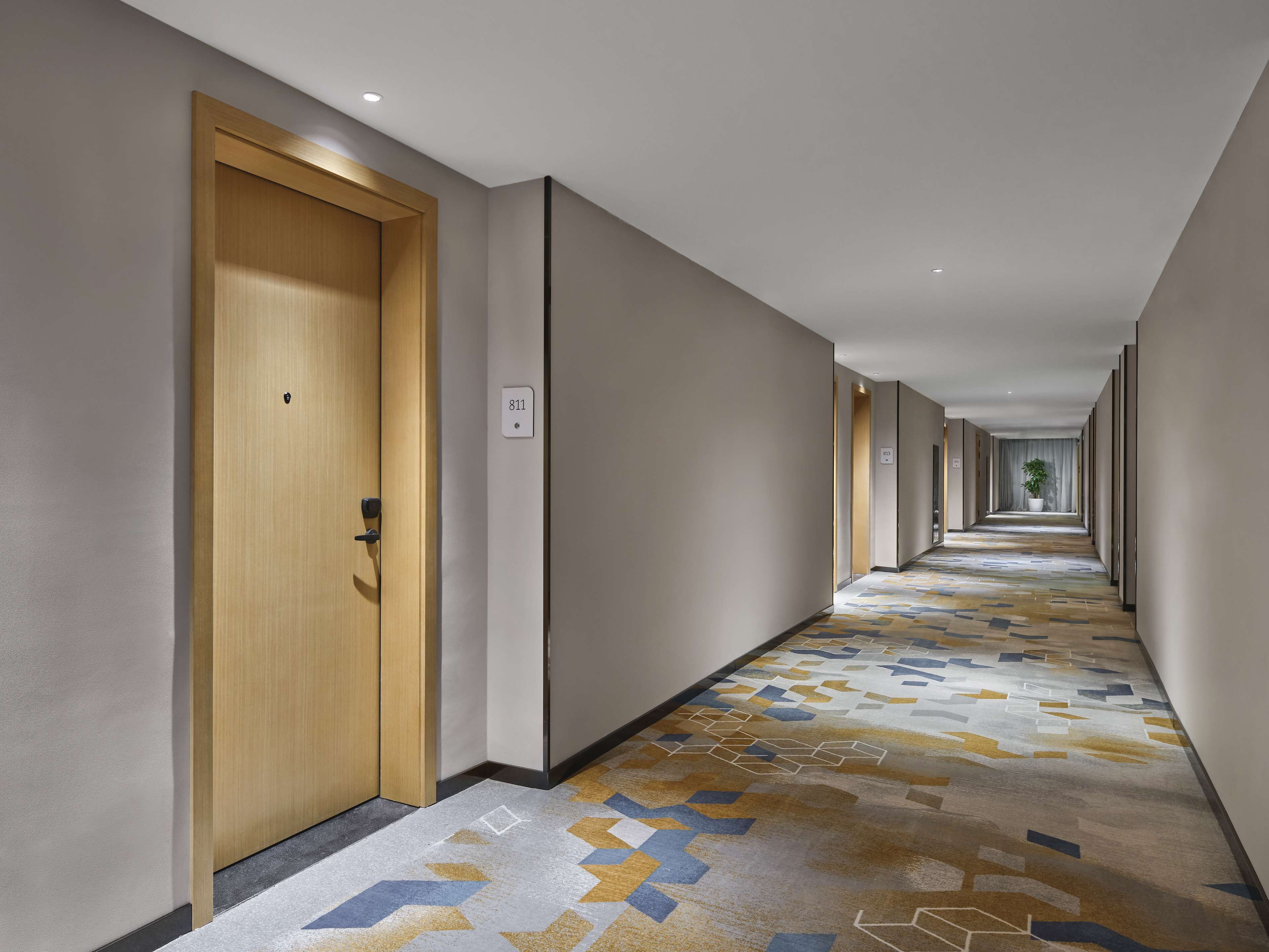 Een hotelgang met vloerbedekking met een patroon, houten deuren en een lange gang.