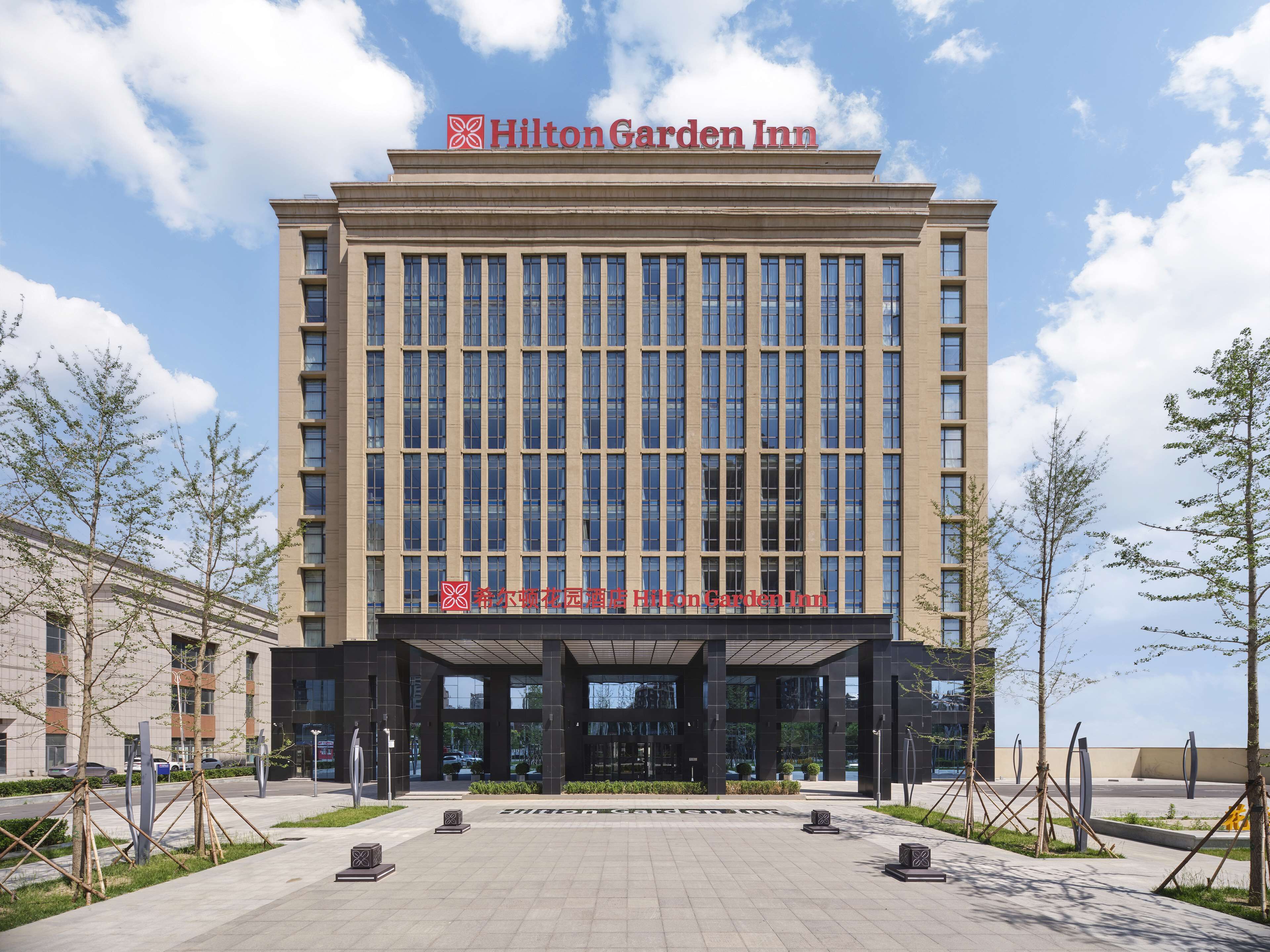 A Hilton Garden Inn building with a modern facade, large windows, and a clear sky.