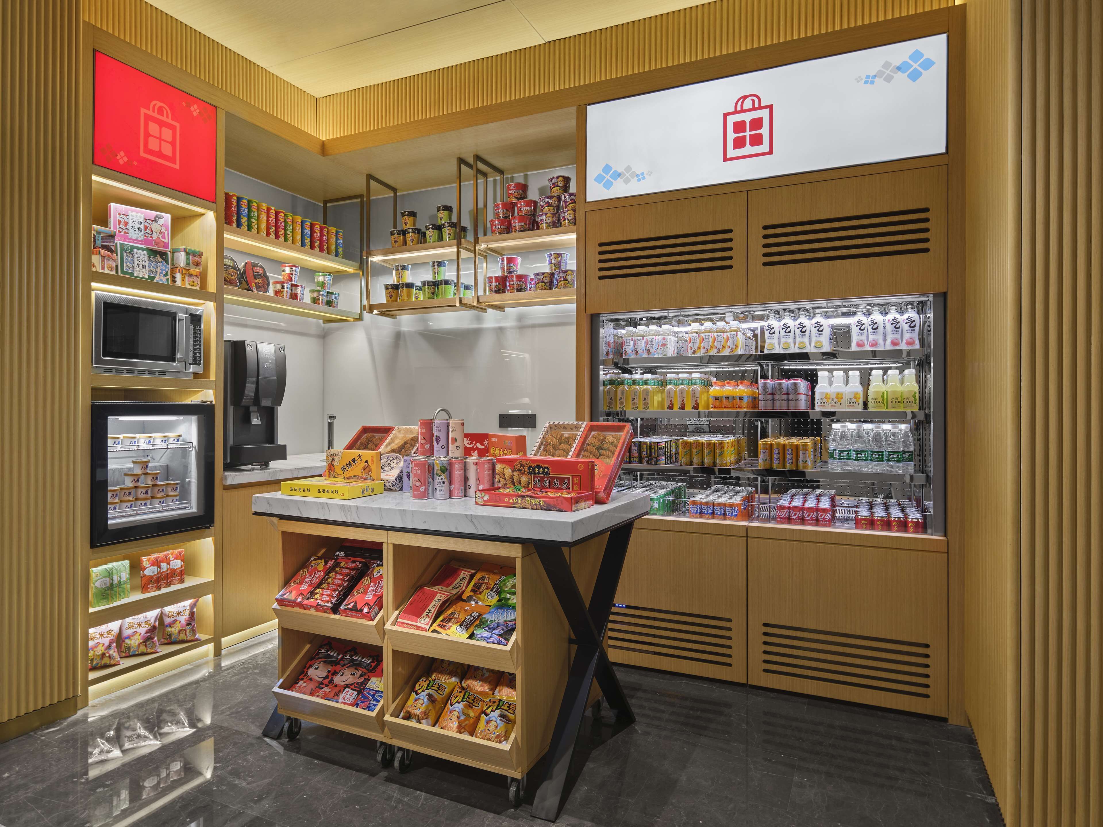Un magasin de détail dont les étagères sont remplies d’en-cas, avec un rayon réfrigéré et un présentoir de boissons en bouteille.