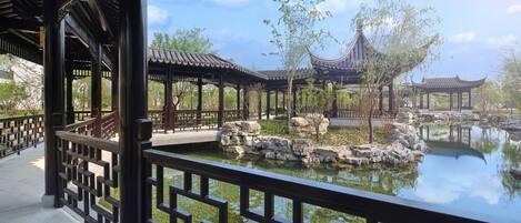 A traditional pavilion with a tiled roof, a stone pathway, and a pond with lily pads.