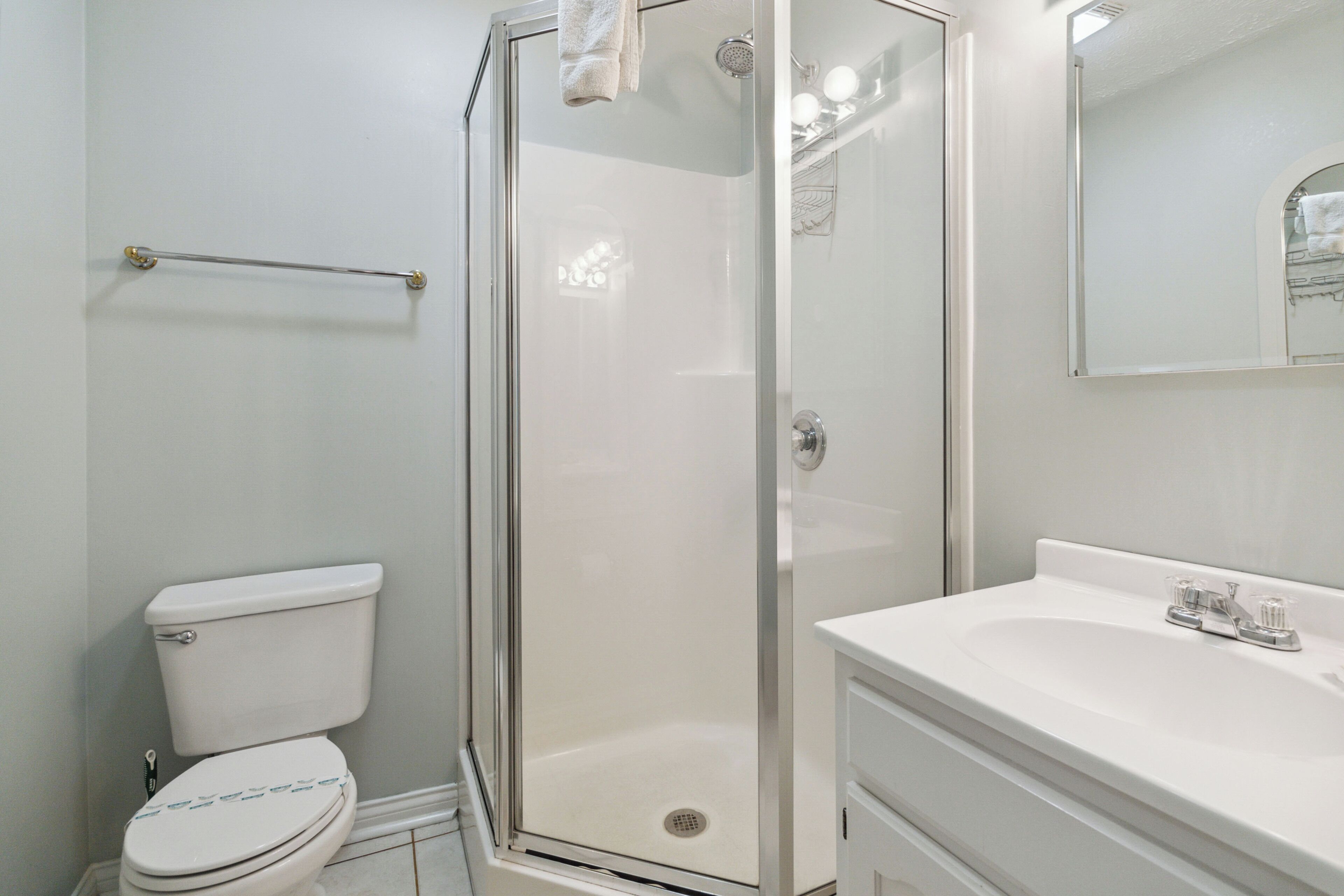 A bathroom with a toilet, a glass-enclosed shower, and a sink with a mirror above it.