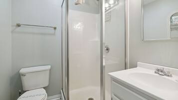 A bathroom with a toilet, a glass-enclosed shower, and a sink with a mirror above it.