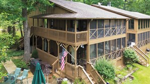 Eine zweistöckige Holzhütte mit Balkon, Sitzgelegenheit im Freien und einer Flagge.