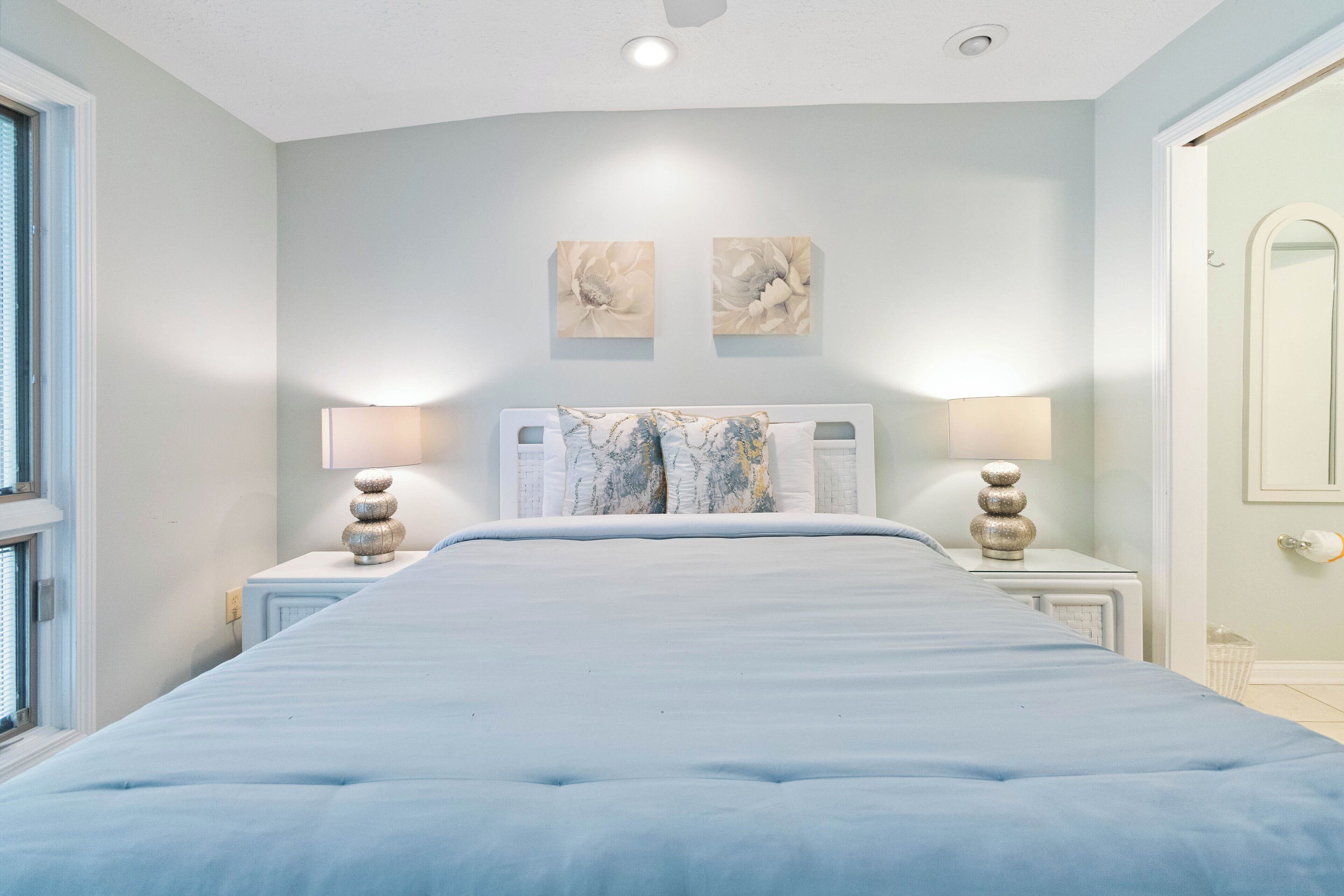 A bedroom with a large bed, two bedside lamps, and artwork on the wall.