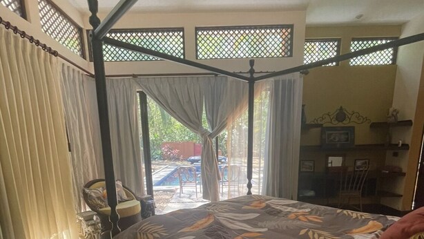 A bedroom with a four-poster bed, a view of the outdoors through large windows, and a dining area visible in the background. - Casa Safari Maganda located in the middle of
paradise. (Tarcoles)