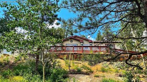 A two-story house with a red balcony, surrounded by trees and vegetation. - Forest cabin on 4 acres,  Newly renovated, Quiet and secluded. (Florissant)