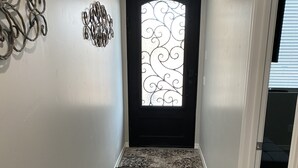 A hallway with a wooden floor, a decorative metal wall piece, and a door with a patterned glass window. - Brand new home,  55 ft garage. 3 bedrooms, sleeps 10.  18ft high garage door.  (Lake havasu)