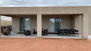 An outdoor patio area with a grill, seating, and a covered table. - Brand new home,  55 ft garage. 3 bedrooms, sleeps 10.  18ft high garage door.  (Lake havasu)