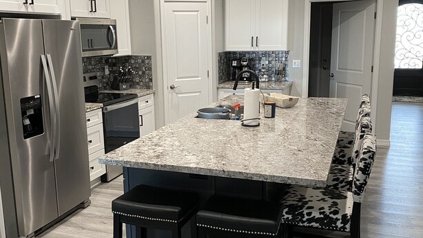 A modern kitchen with a marble countertop, stainless steel appliances, and a bench with a cow print design. - Brand new home,  55 ft garage. 3 bedrooms, sleeps 10.  18ft high garage door.  (Lake havasu)