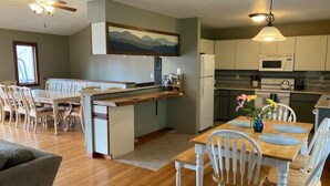 A modern kitchen with white cabinets, a central island, and a dining area with wooden tables and white chairs. - Private Family Mountain Getaway 6mi to Asheville (Fairview)