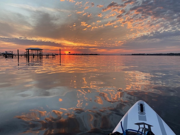 A calm body of water reflecting a sunset with a pier and a boat in the foreground.
