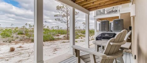 A covered outdoor area with a wooden deck, a table with chairs, and air conditioning units.