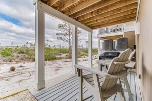 A covered outdoor area with a wooden deck, a table with chairs, and air conditioning units.