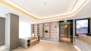 A modern hotel lobby with a reception desk, a seating area, and a wall of display shelves.