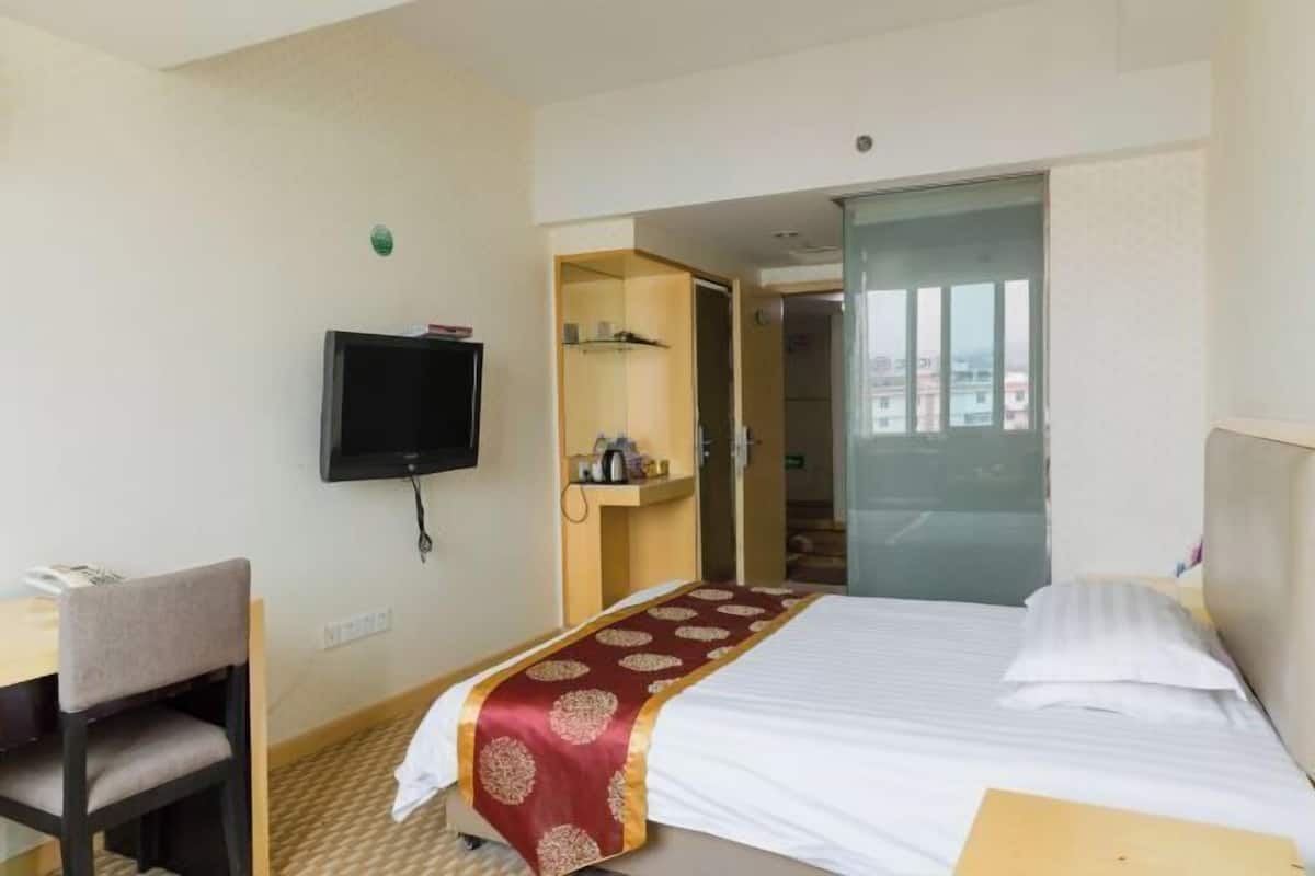Ein Hotelzimmer mit Bett, Schreibtisch, Stuhl, Fernseher und einem durchgegangenen Tür sichtbaren Badezimmer.