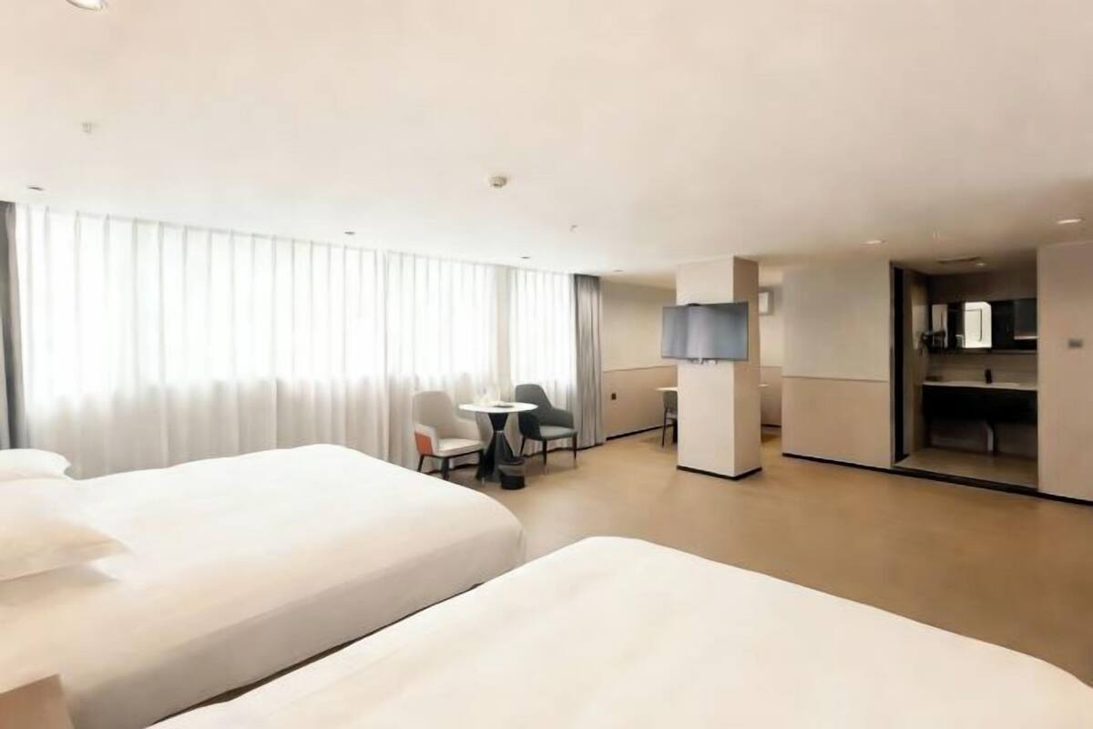 Ein Hotelzimmer mit zwei Betten, einem kleinen Tisch, Stühlen, einem Fernseher und einer Küchenzeile.