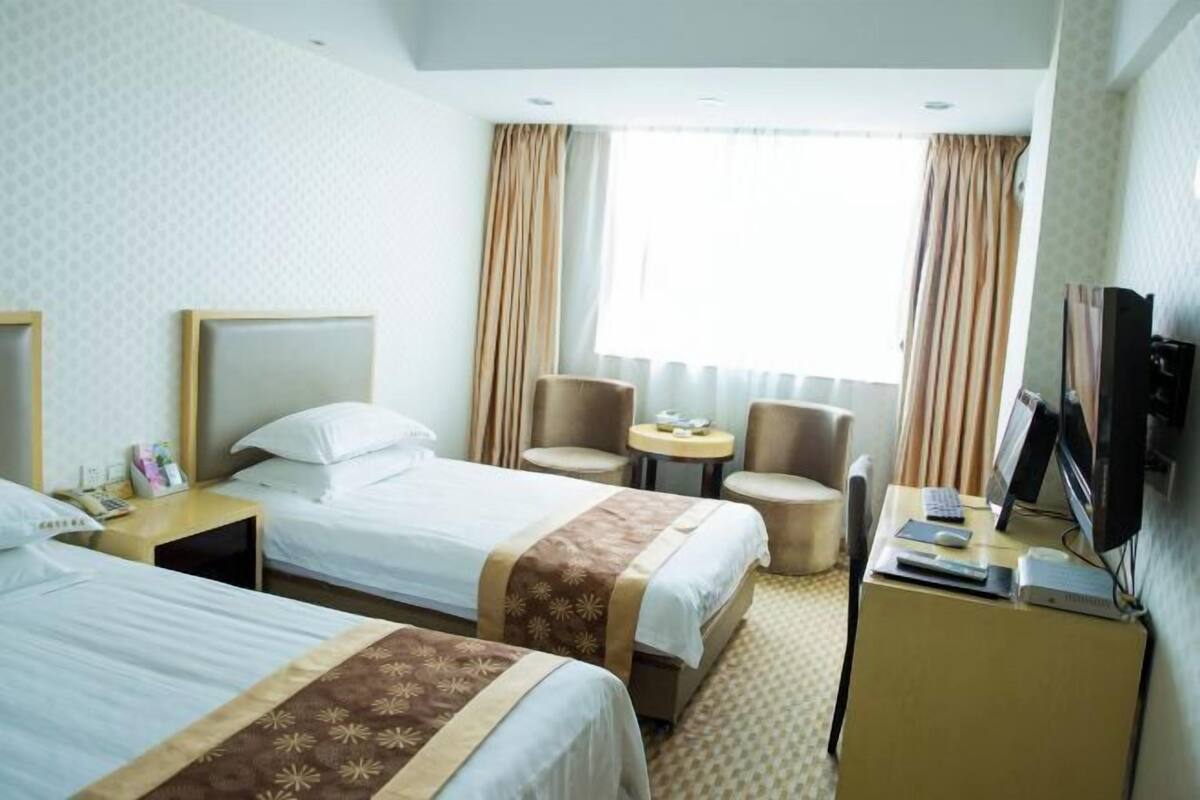 Ein Hotelzimmer mit zwei Betten, einem Schreibtisch mit Computer, einem Fernseher und einem kleinen Tisch mit Stühlen.