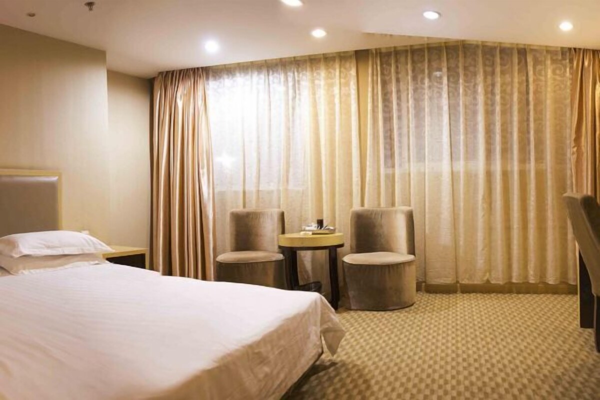 A hotel room with a large bed, two armchairs, a small table, and a desk.