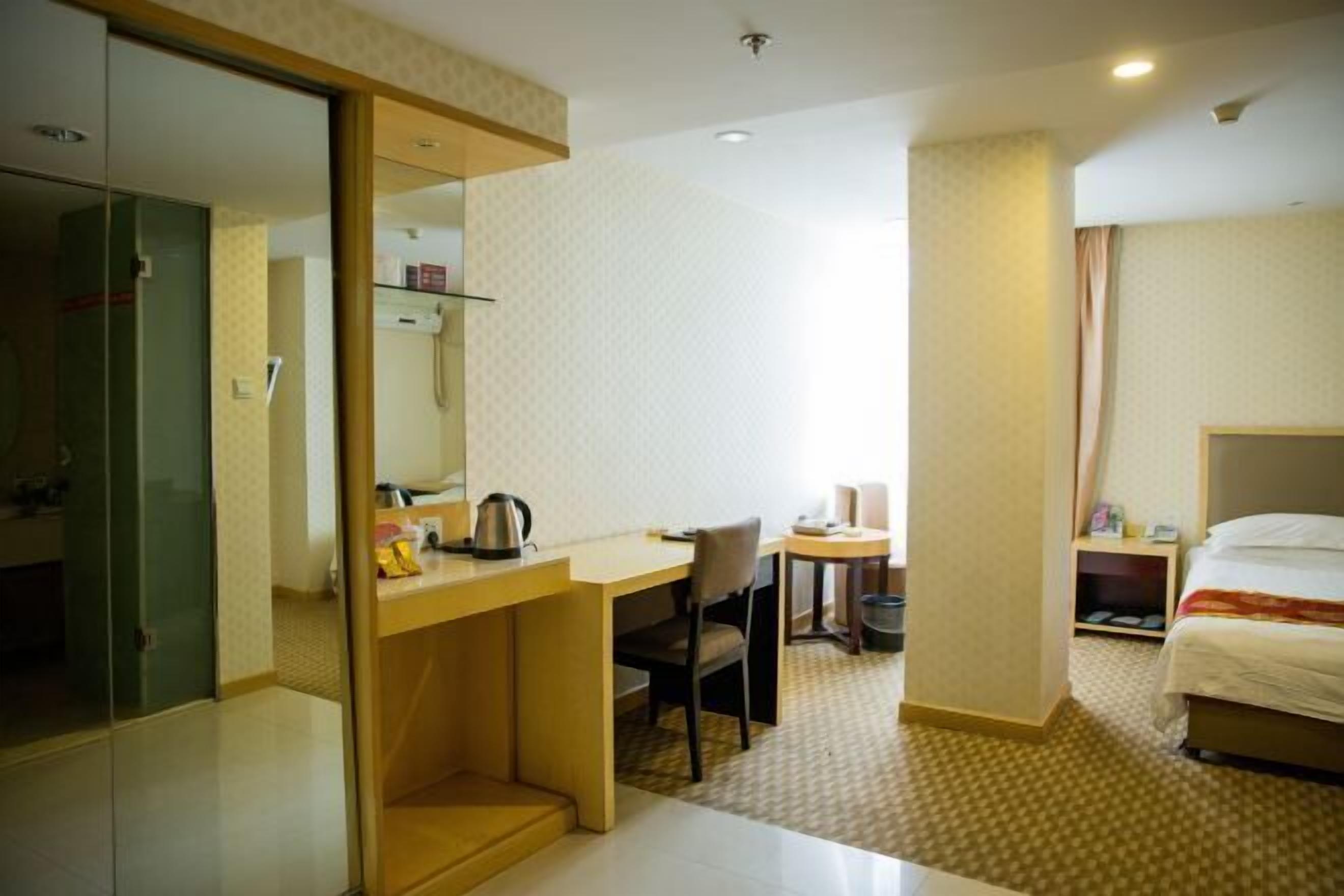 Quarto de hotel com cama, escrivaninha, cadeira, mesinha e espelho.