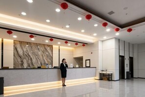Ein moderner Hotel-Empfangsbereich mit Marmorwand, einer Rezeptionistin und roten Laternen an der Decke.