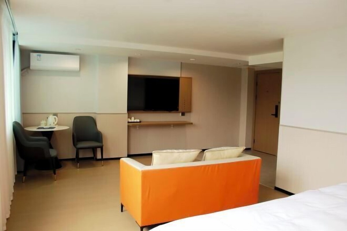 A hotel room with a bed, a TV, a desk with a chair, and a small table with a kettle.