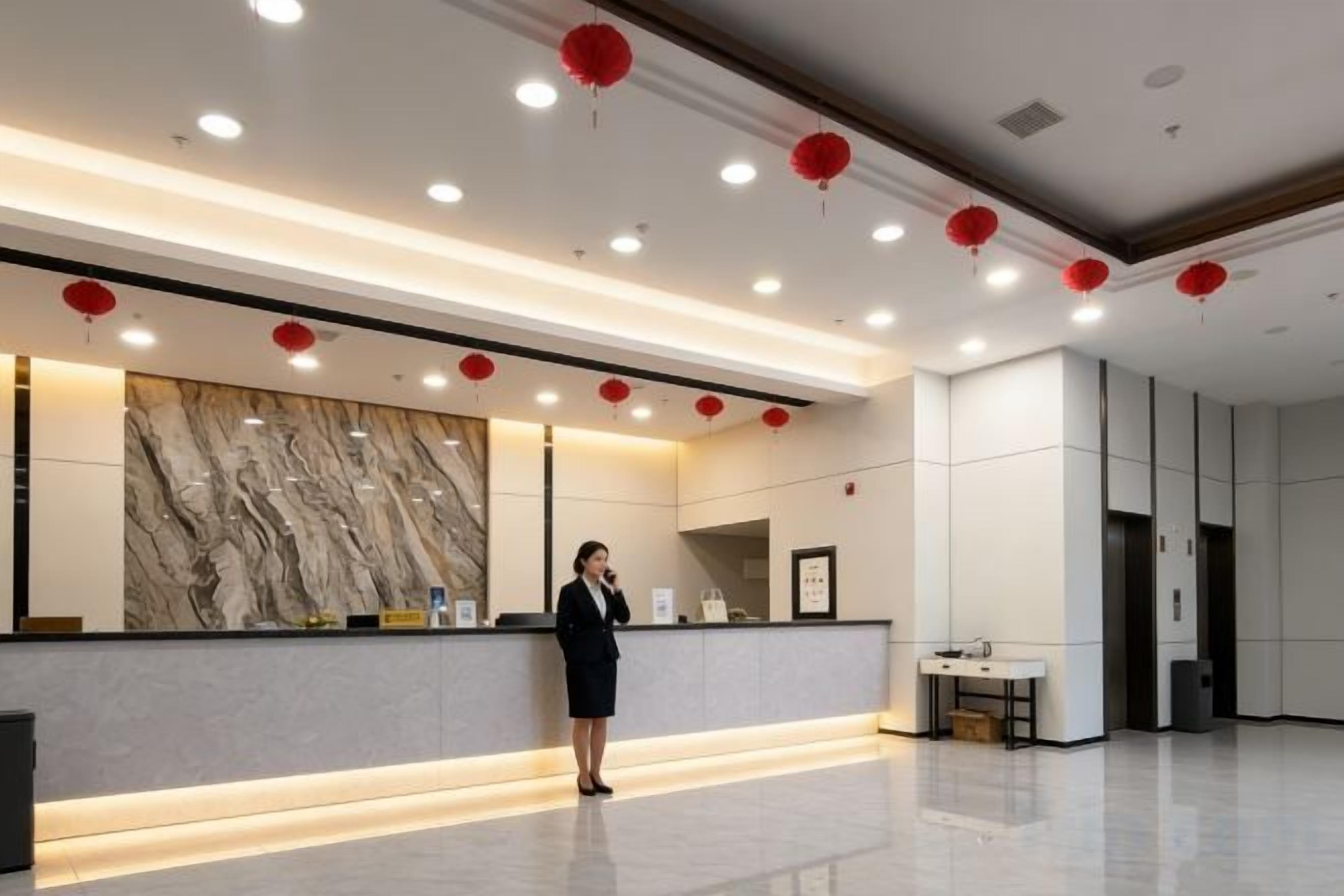 Uma área de recepção de hotel com parede de mármore, balcão de atendimento e lanternas vermelhas no teto.
