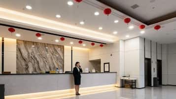 Uma área de recepção de hotel com parede de mármore, balcão de atendimento e lanternas vermelhas no teto.