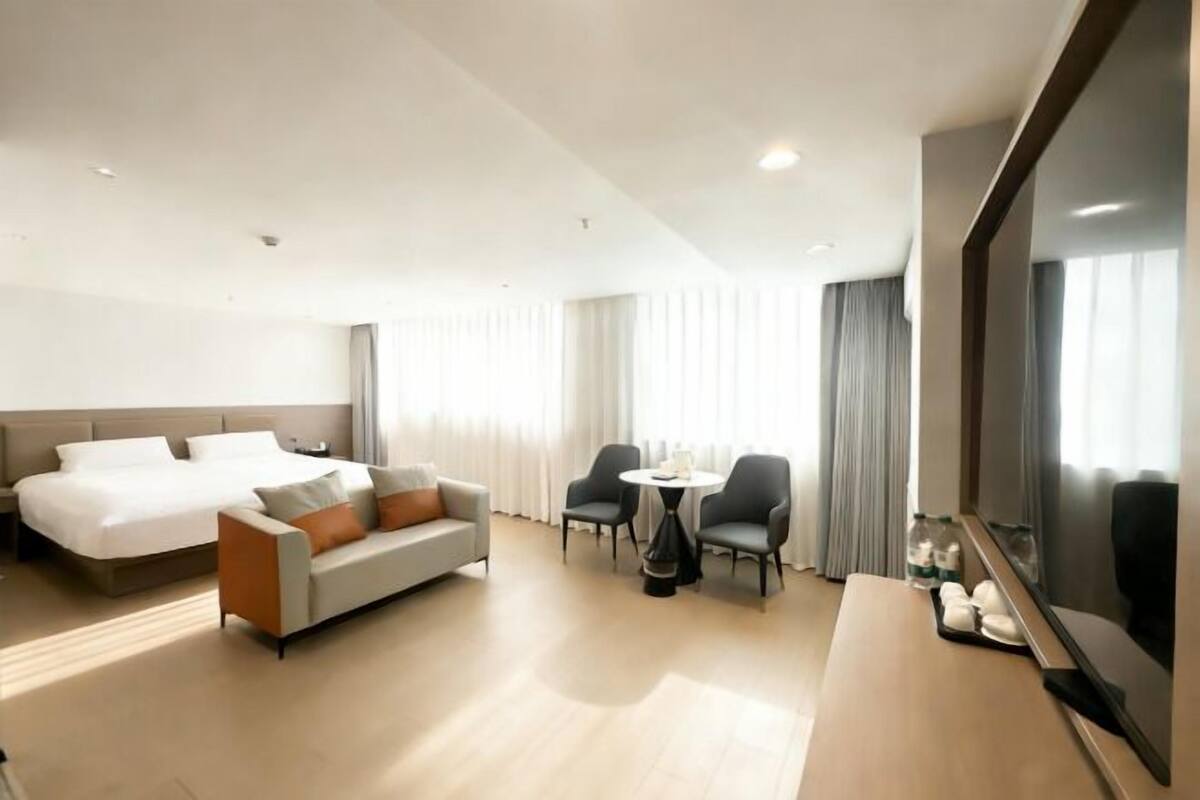 Ein Hotelzimmer mit Bett, einer Couch, einem kleinen Tisch mit Stühlen, einem Fernseher und einem großen Spiegel.