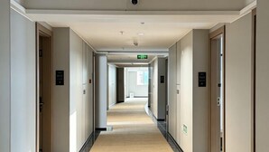 Et hotel med korridor, tæppe på gulvet, døre på begge sider og et loft med indbygget lys.
