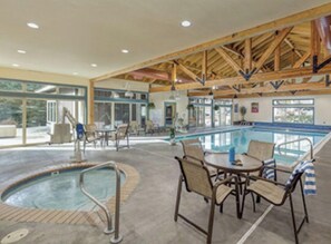 Un espace piscine intérieure comprenant un jacuzzi, des chaises longues et un coin salon abrité.
