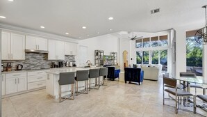 Une cuisine spacieuse avec des meubles blancs, un îlot central doté de tabourets, et un coin repas avec une table et des chaises en verre.