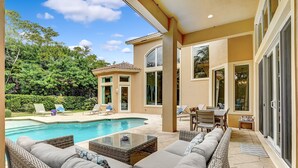 Un espace aménagé au bord de la piscine, avec des meubles en osier, une table en verre et une vue sur la piscine et la végétation environnante.