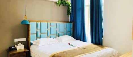 A hotel room with a bed, bedside table, lamp, air conditioning unit, and a window with curtains.