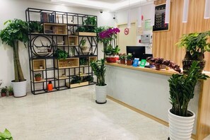A reception area with a wooden counter, potted plants, and a black metal shelving unit. - Impression Boutique Hotel (Shanghai Fengzhuang Metro Station Store) (Shanghai)
