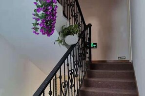A staircase with a black metal railing, a green exit sign, and a potted plant with purple flowers. - Impression Boutique Hotel (Shanghai Fengzhuang Metro Station Store) (Shanghai)
