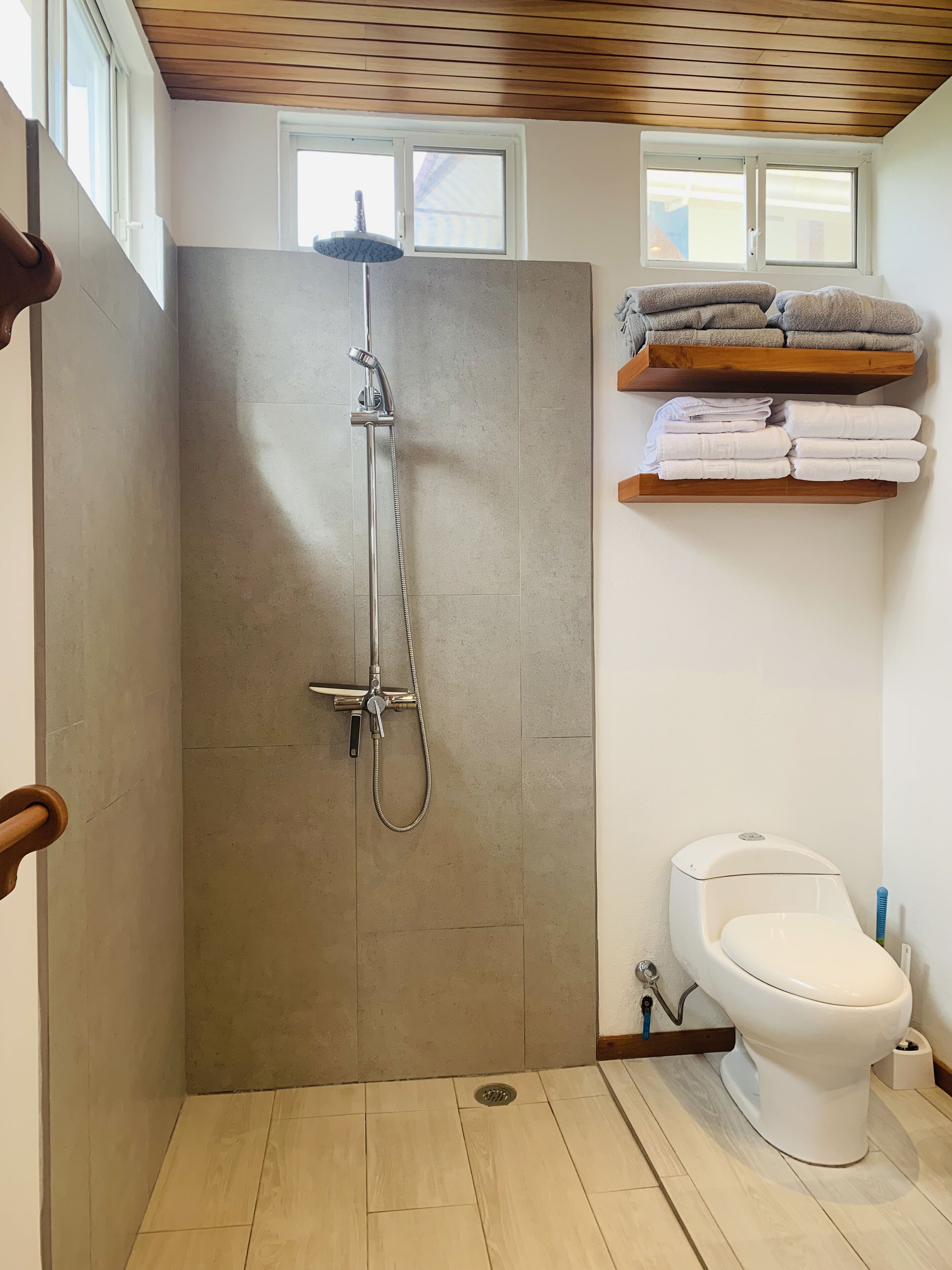 A bathroom with a shower, toilet, and shelves with towels.