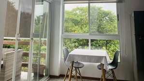Ein Essbereich mit Tisch und Stühlen, großen Fenstern mit Jalousien und Blick auf Grünflächen.