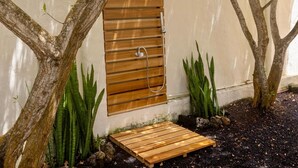 Eine Holztür mit Dusche, umgeben von Bäumen und Pflanzen.