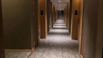 Pasillo de hotel con puertas a ambos lados, suelo alfombrado e iluminación empotrada en el techo.