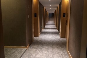 Pasillo de hotel con puertas a ambos lados, suelo alfombrado e iluminación empotrada en el techo.