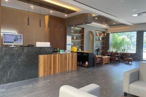 Un área de recepción moderna con mostrador de mármol, detalles de madera y un espacio de estar con sofás.