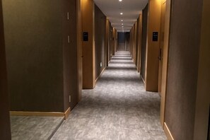 Un largo y estrecho pasillo de hotel con puertas a ambos lados, piso alfombrado e iluminación empotrada.