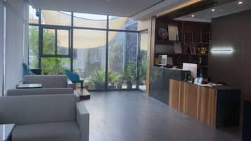 A modern reception area with a reception desk, seating area, and large windows offering a view of greenery.