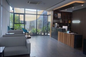A modern reception area with a reception desk, seating area, and large windows offering a view of greenery. - Nanchang 520 Youth Hotel (Mailu Campus Center store of University of Finance and Economics) (Nanchang)